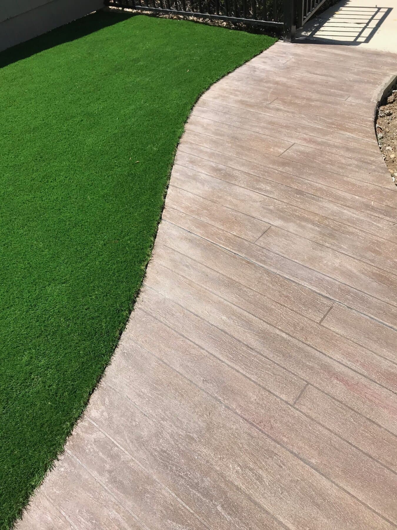 Wood-plank stamped walkway beside turf